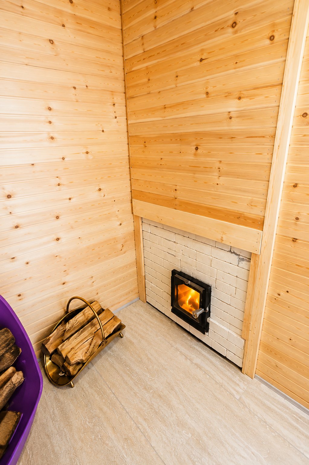 Wood-paneled room with the stove firebox glowing and a basket of firewood